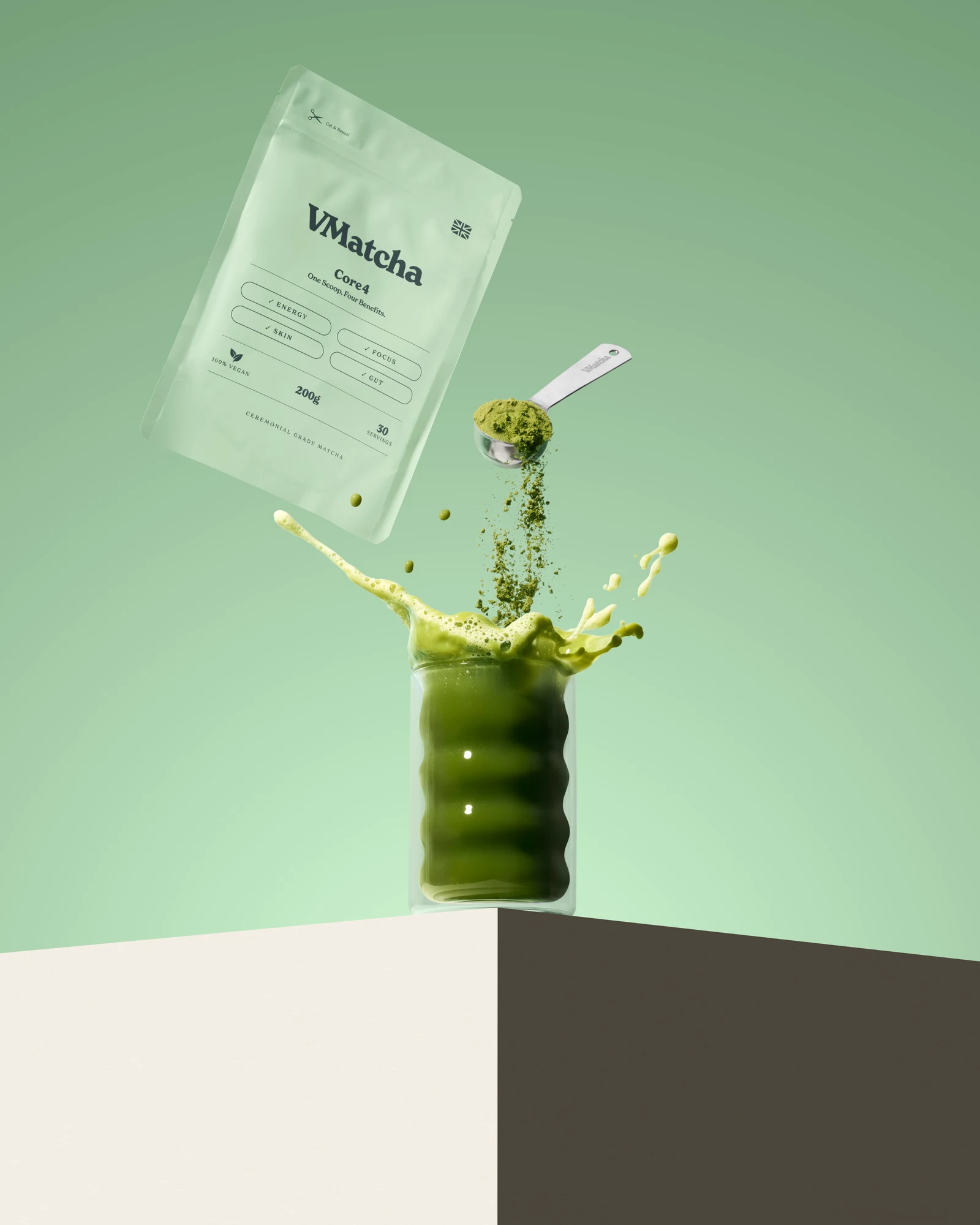 VMatcha Core4 pouch beside a scoop pouring matcha powder into a splashing green drink on a pale green set.