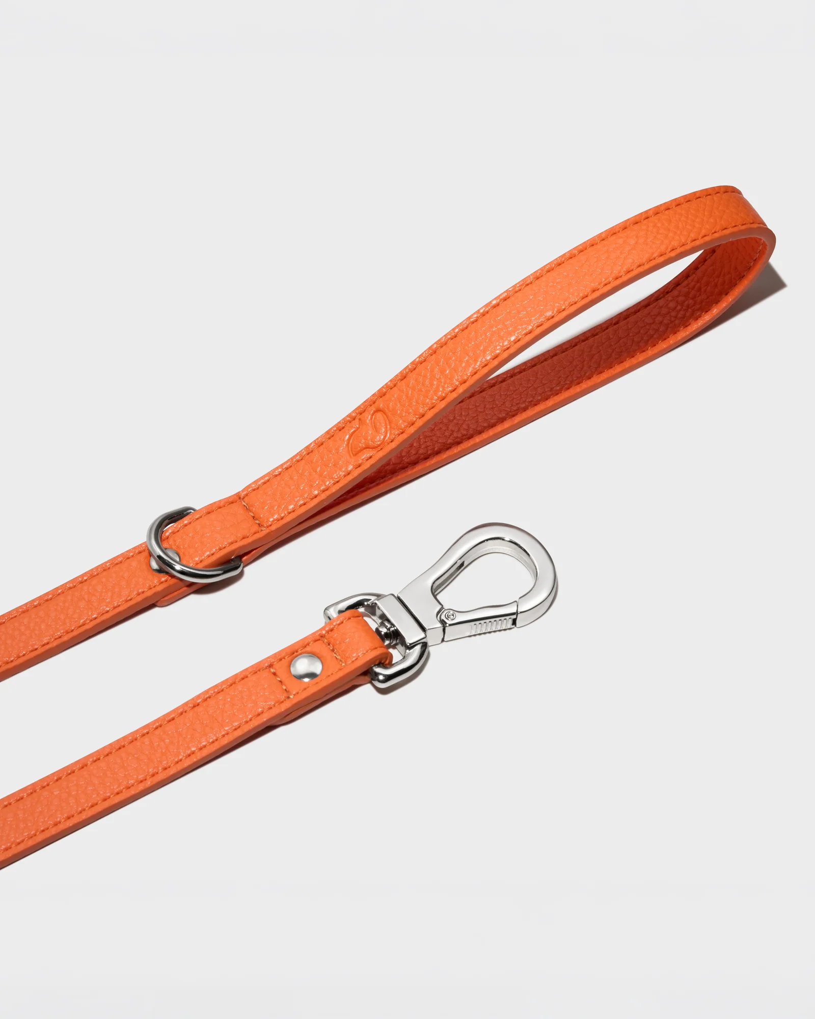 Orange Truffle and Paw leather lead with polished metal hardware on a grey background.