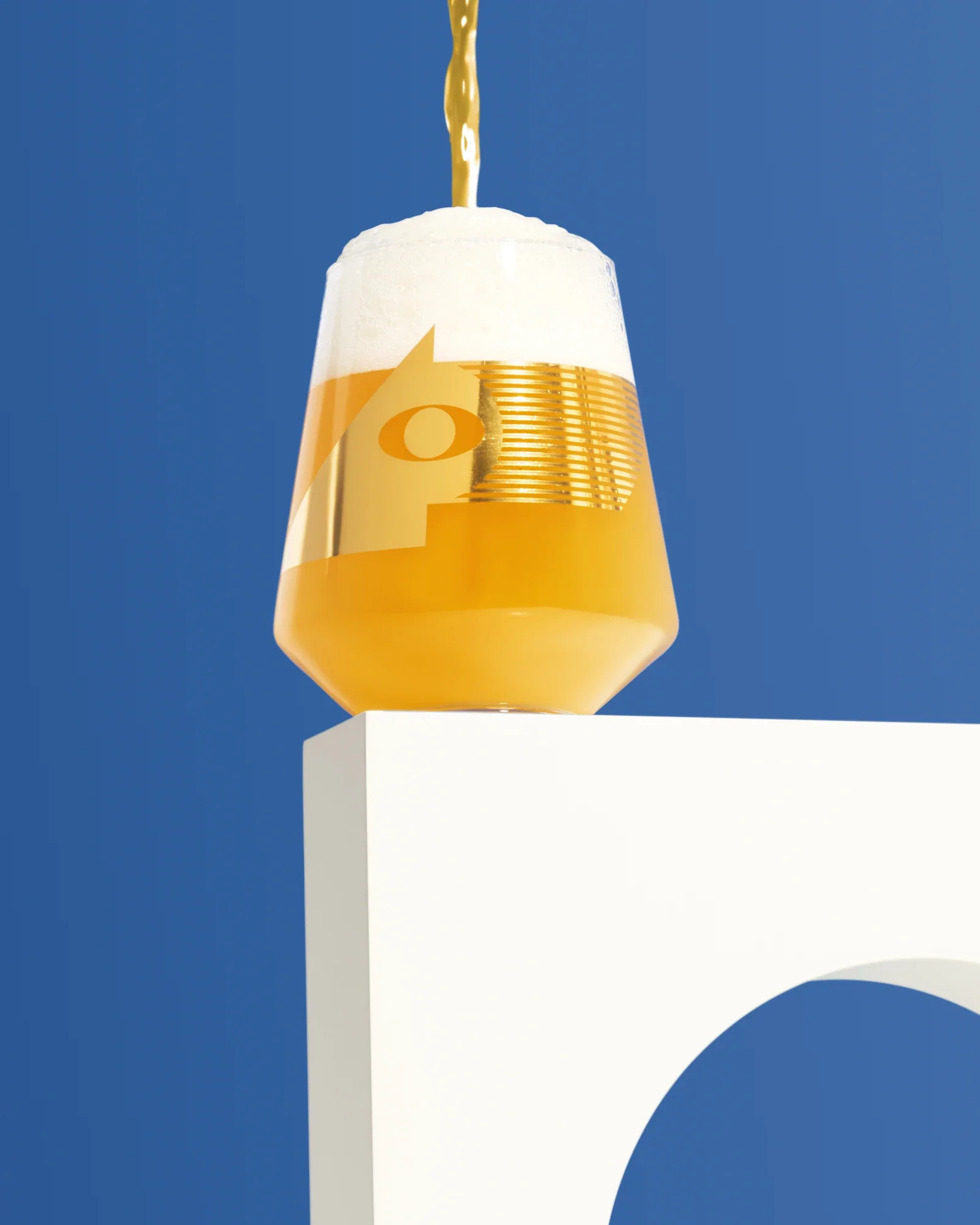 Beer pouring into a Brülo glass on a white architectural plinth against blue.