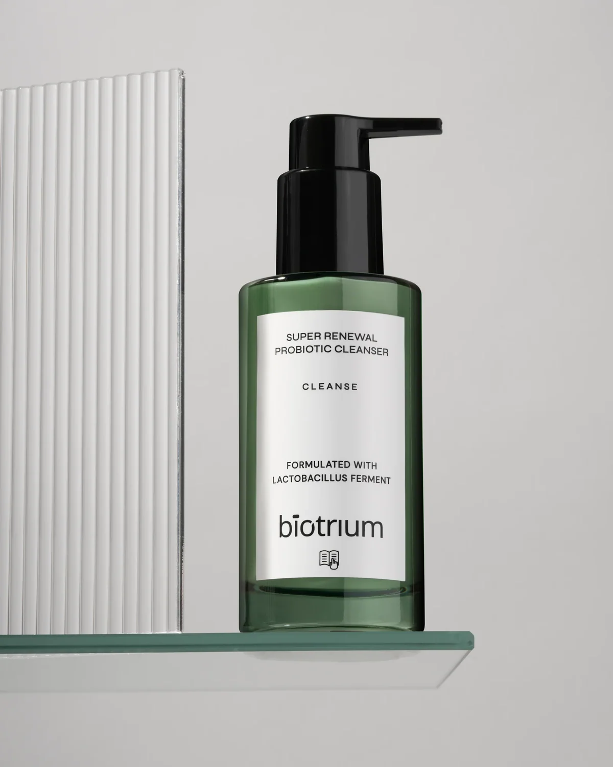 Green Biotrium cleanser bottle on a glass shelf beside a ribbed white panel.