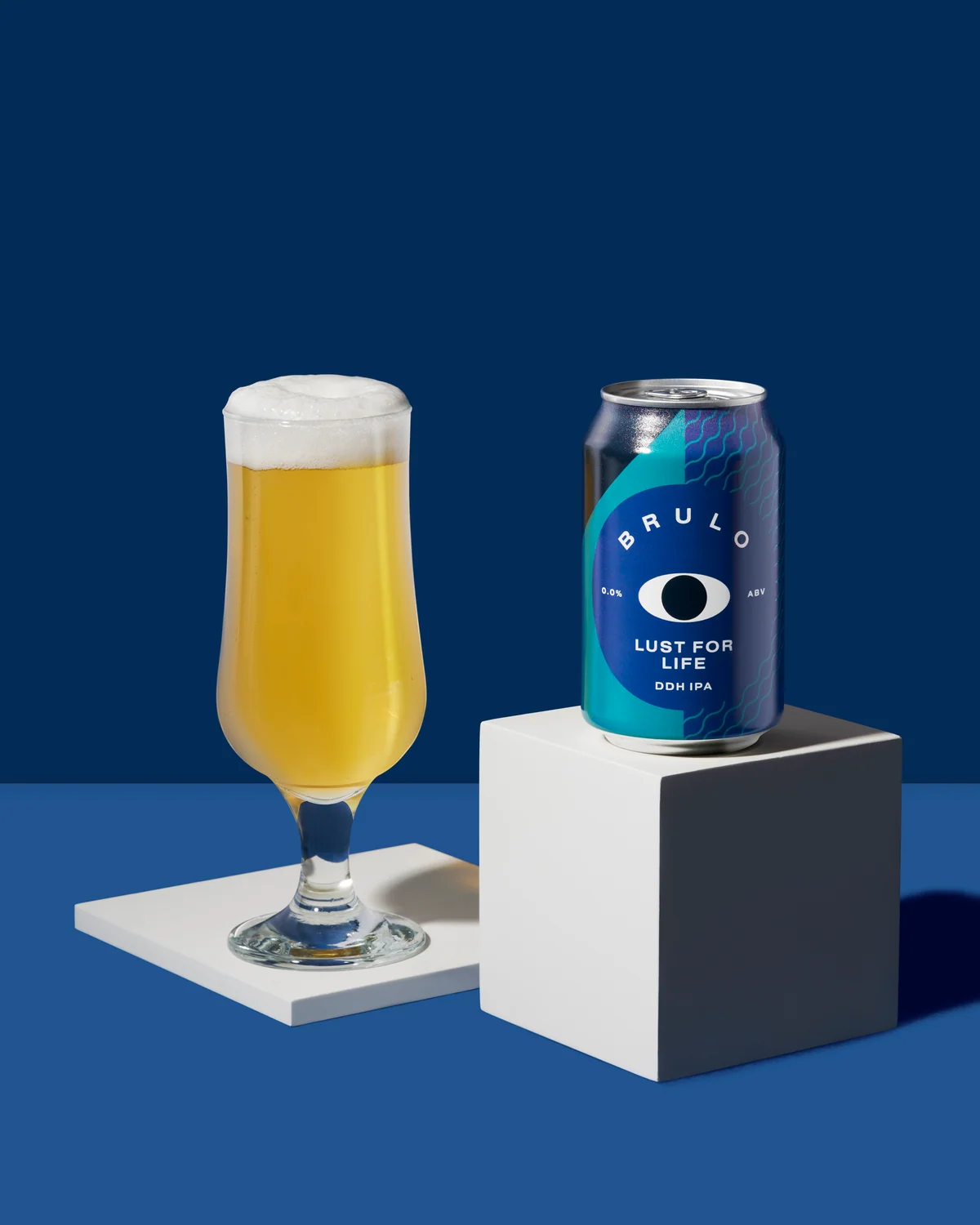 Brülo can and a filled beer glass on white platforms against a blue background.