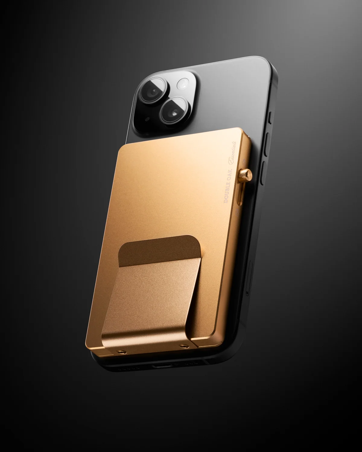 Gold-coloured Double Oak cardholder attached to the back of a phone against a dark background.
