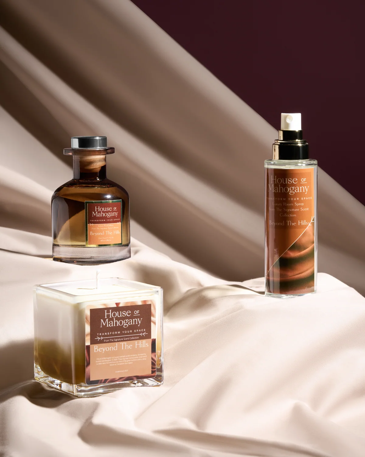 House of Mahogany fragrance bottles arranged on cream fabric in directional light.