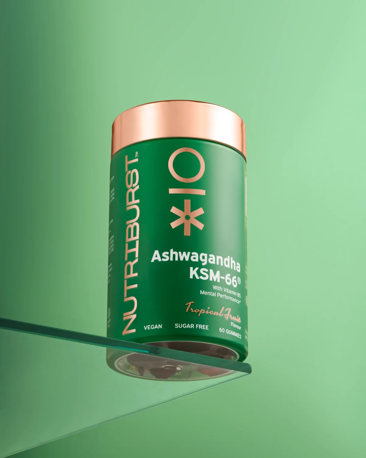 Green Nutriburst jar with a copper-coloured lid on a glass shelf against green.