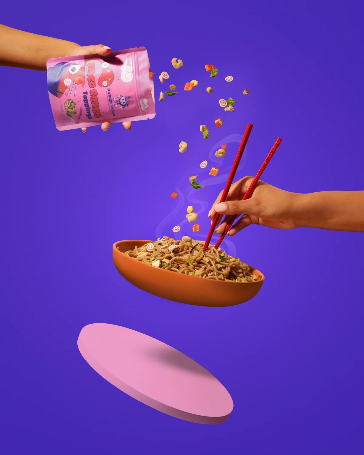 Hands pouring Ramen Bomb toppings towards a bowl of noodles against purple.