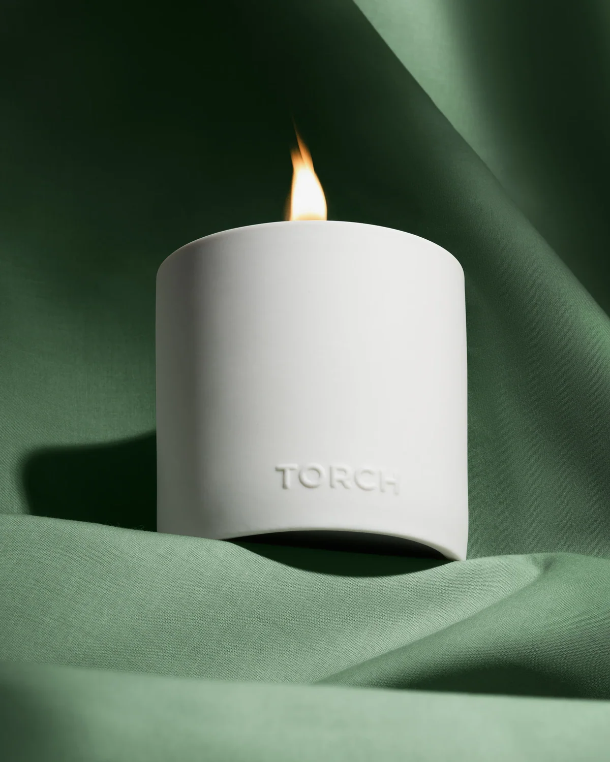 Lit white Torch candle nestled in folds of green fabric.